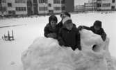 Snögrottor, 4 december 1965.

Man varnar för 'farliga snögrottor' i snöhögarna från snöplogarna. Här bygger barnen en snöfästning på stora cementrör på en fyrkantig innergård omgiven av hyreshus. I bakgrunden snötäckta gungor. En kälke står till vänster.