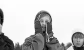 Hästnäs, 20 januari 1966

På bilden syns två flickors ansikten. Centralt i bildens förgrund syns det en flicka som är klädd i vinterkläder. Flickan har vantar på sina händer som hon håller vid sina kinder, handflatorna är vända in mot kinderna. Den andra flickan som syns åt höger i förgrunden har en ljus stickad vintermössa på sitt huvud.