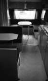 Husvagnar, 26 januari 1966

I bildens förgrund syns en husvagns interiör med  tvättmaskin, spis och kylskåp åt höger och ett bord åt vänster. I bilden bakgrund syns det en hörnsoffa runt bordet och högst upp centralt på bilden syns det en taklampa.