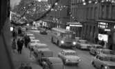Julrusch, 24 december 1965

Bild av norra delen av Drottninggatan mot Storbron. Granrisgirlander med lampor och julprydnader i form av gula stjärnor och röda klockor hänger i bågar tvärs över gatan med ca 10 m avstånd mellan. Trottoarerna är fyllda med folk.