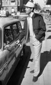 Andersson Gustavsson mode 23 april 1966

En manlig fotomodell visar herrkläder. Han är iklädd jacka, skjorta, byxor samt hängslen. PÅ huvudet har han en hatt. Han håller i ett par handskar i sin högra hand samtidigt som han öppnar en bildörr på en parkerad bil. Hus och bilar syns i bakgrunden.