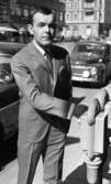 Andersson Gustavsson mode 23 april 1966

En manlig fotomodell visar herrkläder. Han är iklädd kostym, skjorta och slips. Han står utomhus på en gata och håller sin högra hand på en parkeringsautomat. Bilar och hus syns i bakgrunden.