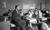 Engelsk lärare 6 april 1966

En lärare i engelska sitter på en skolbänk och blickar ut över och undervisar eleverna i sin klass.










































































































or. Han går nedför en kort trappa utomhus.