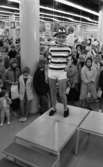 Baddräkter 12 maj 1966

En fotomodell klädd i randig tröja, vita shorts, svarta skor samt med en mönstrad hatt på huvudet står på catwalken. Nedanför i bakgrunden står publik.
















































































































or. Han går nedför en kort trappa utomhus.