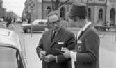 Värdinnor på enkät 13 maj 1966

En värdinna klädd i dräkt och hatt. Hon håller i ett block med ett papper med trafikmärken på med vänster hand. I höger hand håller hon en penna. En man iklädd kavaj,slips, skjorta och glasögon står bredvid. De står tillsammans vid en parkerad vit bil. I bakgrunden kommer en bil som är på väg att göra en vänstersväng. Före denna kör två personer på mopeder. Ytterligare personer och fordon står i bakgrunden.





















































































































or. Han går nedför en kort trappa utomhus.