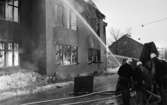 Noraskola brinner 18 februari 1966

Det brinner i en skola i Nora en vinterdag. Fyra brandsoldater i branduniformer och hjälmar står framför byggnaden och har riktat en brandspruta mot husfasaden. En man i vardagskläder står mitt i gruppen av brandmän.