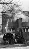Noraskola brinner 18 februari 1966

Det brinner i en skola i Nora en vinterdag. Fyra uniformerade brandmän och en civilkläd man syns stående vid sidan av vattenpump. En av brandmännen har riktat ett vattenstråle mot skolbyggnads fasad. Det syns rökutveckling på skoltaket.