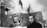 Nora-branden efteråt, 19 februari 1966

I förgrunden syns det en man som är klädd i en mörk rock. I bakgrunden skymtar det som är kvar av byggnaden efter brand. Istappar hänger från byggnaden.