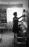 Fru Ring 15 januari 1966

Medelålders kvinna poserar vid mindre hylla med prydnadssaker