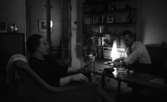 Brudpar 1946 (hemma hos), 9 mars 1966

En kvinna sitter i en fåtölj i ett vardagsrum. Hennes man sitter mittemot henne i en soffa. På ett bord som står emellan dem ligger bl.a. ett askfat samt en glasskål med lock. En golvlampa lyser i bakgrunden. Bkom denna syns en bokhylla invid väggen.
