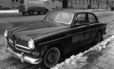 Bilar, Bilnummer, Bilhall 30 mars 1966En bil står parkerad vid en gata. En skåbil kommer körande i bakgrunden. En dam syns på trottoaren mittemot.