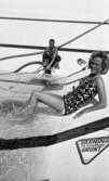Hej Sommar, Bilskola 3 maj 1966

En kvinna i baddräkt sitter på kanten till en simbassäng i Gustavsviksbadet. I bakgrunden syns en man som håller i en vattenpump. Till höger om kvinnan syns en skylt infogad i bassänkanten där det står: 