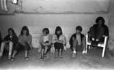 Oläslig rubrik 23 augusti 1965
 
Fem tonåringar sitter på golvet i en källarlokal. En kille sitter i en vit stol till höger.