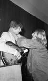 Popgala i Kumla, Farlig skolväg 24 augusti 1965

En närbild på en rockgitarrist i randig kavaj och slips som omfamnas av en tonårsflicka klädd i jacka. Hon håller sina händer runt hans nacke.