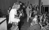 Popgala i Kumla, 24 augusti 1965

Ett rockband spelar i Kumla på en scen. Två av bandmedlemmarna har gitarrer i sina händer. En tredje medlem spelar på tamburin. En sångare med Sherlock Holmesinspirerad hatt står i mitten av scenen framför en mikrofon. I bakgrunden syns ett piano. Publiken står nedanför scenen. En tonårsflicka i publiken har en marackas i sina händer.