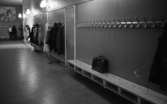 Väsktjuvar, Malmströms, Studenten 2, Väsktjuvar 20 april 1966

I en korridor står en portfölj på en avlång träbänk. I korridoren finns fyra dörrar och mellan dessa finns rader med krokar där människor har hängt sina kappor och rockar. I bakgrunden syns tre personer som står och samtalar. Ovanför dem hänger en tavla på väggen.