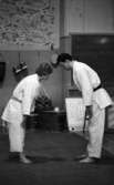 Julreportage, United Shoe 3 februari 1966

Två män klädda i judokläder bugar sig för varandra. I bakgrunden finns en svart tavla där det står med krita: 