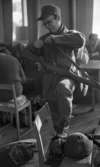 Rycket in i lumpen 8 februari 1966

En soldat står inne i en stor sal med vänster fot på en stol. Han sysslar med axelremmen till sitt gevär. I bakgrunden syns två andra soldater.