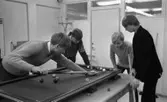 Biljard fritidssysselsättning 1 februari 1966

Fyra unga pojkar spelar biljard i ett rum. Pojken längst till vänster håller på att skjuta iväg en boll. De andra betraktar detta koncentrerat. Biljardbordet står ovanpå ett annat bord. Tre av pojkarna är klädda i tröjor och den fjärde bär kavaj. En klädhängare står i bakgrunden.