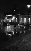 Vårregn, 31 januari 1966

Utanför Centralstationen en mörk, regnig vinterkväll. Två bilar står parkerade utanför byggnaden. Tre personer är också med på bilden. Det ligger även snö på marken.