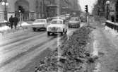 Vårregn, 31 januari 1966

Bilar kör på gatan i centrala Örebro. I bakgrunden ligger Stora Hotellet. Det ligger snö på trottoaren. Tre herrar i mörka rockar och hattar syns i bakgrunden på bilden samt ytterligare personer längre bort.