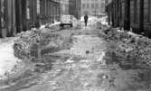 Vårregn, 31 januari 1966

På en gata med byggnader runtomkring kommer en man gående. En vit bil står parkerad vid trottoaren till vänster. Det ligger snö på marken.