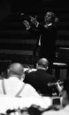 Cellibedache 13 juni 1966

En dirigent klädd i vit skjorta och svart kavaj viftar med taktpinnen framför en orkester. Framför honom sitter musiker och spelar.