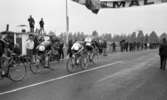 Cykel, 6 juni 1966

Ett antal cyklister cyklar in i mål under en tävling. Publik står på båda sidor om vägen och tittar på. Två svenska flaggor står uppställda vid var sin sida om vägen. Över vägen hänger en skylt med texten: 