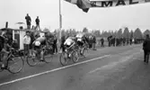 Cykel, 6 juni 1966

Ett antal cyklister cyklar in i mål under en tävling. Publik står på båda sidor om vägen och tittar på. Två svenska flaggor står uppställda vid var sin sida om vägen. Över vägen hänger en skylt med texten: 