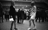 Popgala 6 juni 1966

Närbild på två unga flickor. Flickan till vänster är klädd i svart klänning, svartvita lågklackade pumps och bär en vit handväska i sin högra hand. Flickan till höger har vit ärmlös blus, vit kjol, vita stövlar samt bär en vit handväska på höger arm. I bakgrunden syns andra personer.