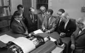 Datamaskin 28 maj 1966

Åtta herrar klädda i skjortor, slipsar och kostymer står intill en stor datamaskin i ett rum och diskuterar skriften på ett papper som kommit ur maskinen. Hyllor syns på väggarna i bakgrunden.