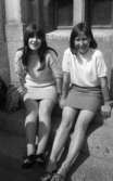 Korta kjolar 15 juni 1966

Två unga flickor sitter på en trappa framför två fönster en solig sommardag. De är klädda i kortärmade blusar, korta kjolar och sommarskor.