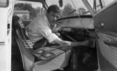 Beg. bilar, Ferieskola, Bodenkille slog rekord 14 juli 1966

En ung man sitter i framsätet i en vit bil och håller sin högra hand på bilradion där han är i färd med att skruva på en knapp. I sin vänstra hand håller han i en högtalarmikrofon. Han är klädd i vit skjorta.