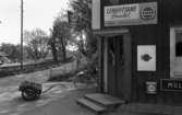 Lekhyttan 21 juni 1966

Närbild på entrén till Lekhyttans lanthandel. En cykel står parkerad vid cykelstället bredvid. En kärra fylld med flaskor står på marken. En skylt där det bl.a. står 