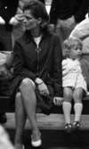 På stationen 1 16 augusti 1966

En liten flicka i kort, ljus klänning, mörk kofta, vita strumpor och mörka skor sitter bredvid sin mamma som är klädd i vit, kort klänning, mörk kappa och vita skor på en bänk på Örebro järnvägsstation.