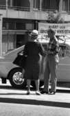 Strosor rep 2 25 juli 1966

En äldre kvinna i mörk, prickig klänning samt en vit hatt på huvudet står med ryggen mot kameran och samtalar med en äldre herre klädd i rutig skjorta och ljusa byxor som står vänd mot kameran. I bakgrunden står en bil.