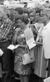 Missionsläger 10 augusti 1967

På ett missionsläger står en grupp kvinnor och män och lyssnar tillsammans. De har små böcker i sina händer som bär titeln 