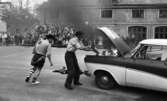 Mosåsflicka, Brandkårsuppvisning, Harar, Transportkillar 27 maj 1967

Två män klädda i maskeradkläder är i färd med att släcka en eldsvåda i motorhuven på en bil. Den ene mannen är klädd i skjorta, shorts, strumpor och skor och den andre mannen håller i en brandspruta och sprutar in i motorhuven. Han är klädd i skjorta, byxor, hatt och skor. Publik åser det hela i bakgrunden.