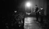 Natt 702, 12 juni 1967

Jokkmokks-Jokke står på en scen och sjunger samt spelar gitarr klädd i samedräkt. En annan man klädd i kostym spelar dragspel bredvid honom. Publik står nedanför scenen och tittar på.
