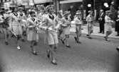 Marknadsafton 16 juni 1967

En orkester går gatan fram i centrala stan i Örebro. Den består av både kvinnor, män och ungdomar. Kvinnorna bär kavajer och kjolar och männen bär kavajer och byxor. En tamburmajor- en kvinna går framför gruppen med musikinstrument i händerna. Affärer och byggnader samt åskådare syns i bakgrunden.