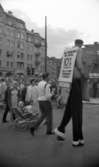 Marknadsafton 16 juni 1967

Under en marknadsafton går en man på styltor och med en reklamskylt på sig där det står: