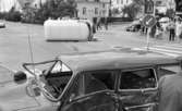 Krock 26 juni 1967

En vit buss ligger på sidan på gatan nära en refug i bakgrunden. I förgrunden syns en svart bil med intryckt sidodörr och saknad framruta. Båda fordonen har varit med om en krock. I bakgrunden till höger syns vuxna med två cyklar samt barn som betraktar olycksplatsen.