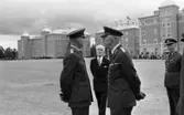 Kungen I3 28 augusti 1967

Kung Gustav VI Adolf besöker Örebro Livregementes Grenadjärer i Grenadjärsstaden. Ett antal män står uppställlda på regementsgården klädda i militäruniformer liksom kungen. Den sistnämnde står och samtalar med en general. En man i svart kostym, vit skjorta och ljus slips syns i bakgrunden.