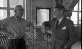 Kembels slutar, Blå stjärnan, 8 juli 1967

Två män står inne i en skofabrik. Mannen till vänster är klädd i vit, rutig skjorta och mörka byxor. Den andra mannen bär mörk, rutig kostym, vit skjorta och mörk slips. De lutar sig mot skohyllor medan de står upp och samtalar.