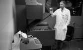 Lasarettet 14 juni 1967

En läkare står vid en låda fylld med medicinska flaskor inne i ett rum. Han lyfter på lådans lock och visar innehållet Han är klädd i vit läkarrock, vit skjorta och mörk slips. En maskin står i förgrunden. En fåtölj står i bakgrunden.