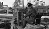 Frövi 2 juni 1967

En järnvägsarbetare kör truck på Frövi järnvägsstation klädd i arbetsoverall. Ett tåg lastat med timmer syns i bakgrunden.