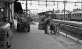 Frövi 2 juni 1967

Två järnvägsarbetare på Frövi järnvägsstation. Den ene håller på att pumpa upp det bakre cykeldäcket med en cykelpump och den andre sitter på huk bakom cykeln och sätter i pumpslangen i ventilen. En truck står i bakgrunden. Två andra vagnar syns också på bilden.