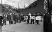 Första maj demonstration 2 maj 1967

Ett stort antal män står i ett första-majtåg i centrala Örebro. De är klädda i rockar, byxor och skor. I förgrunden står en man och håller i en trästång i ena hörnet av en stor banderoll. På denna står texten: 