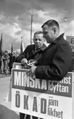 Första maj demonstration 2 maj 1967

Två män står i ett första-majtåg i centrala Örebro. De är klädda i rockar, byxor och skor. De håller i skyltar med texten: 