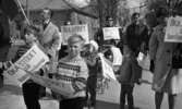 Första maj demonstration 2 maj 1967

Ett första-majtåg går igenom centrala Örebro. På bilden syns ett antal barn som kommer gående i tåget. Två pojkar i förgrunden håller varsin skylt med texten: 